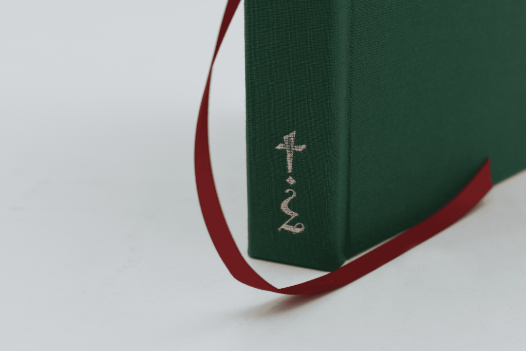Detail shot of the spine of a green book with a gold glyph on the spine, framed by a red ribbon on a white background